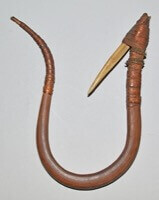 Un mince morceau de bois est courbé en forme de "U" avec une courbe à une extrémité et une défense pointue dirigée vers l'intérieur à l'autre extrémité. La défense est attachée à du cuir et à de la ficelle. L'autre extrémité est entourée de cuir pour tenir une ligne.